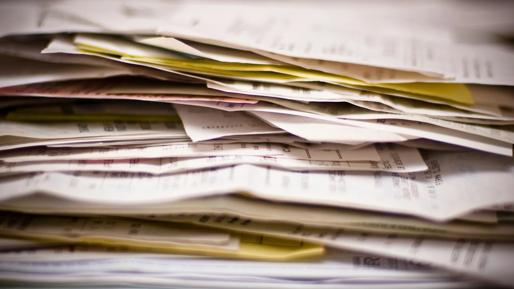 A thick stack of paper receipts and invoices seen edge on
